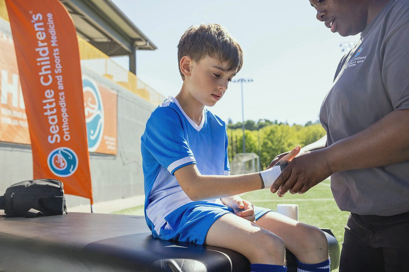 An athletic trainer wraps a young soccer player’s wrist on a turf field.
